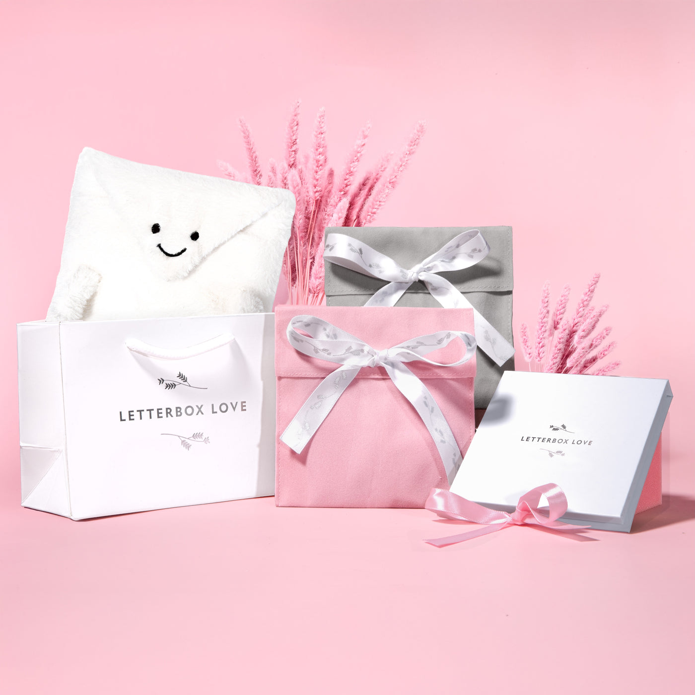 Gift boxes with ribbons and 'Letterbox Love' packaging on a pink background