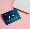 A pair of star-shaped earrings attached to a dark blue card with the text, 