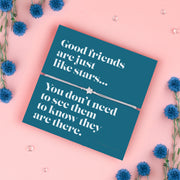 A silver-plated star charm bracelet on an adjustable cord, displayed on a teal backing card with the message: "Good friends are just like stars… You don’t need to see them to know they are there." Surrounded by blue flowers on a soft pink background. Perfect for gifting.