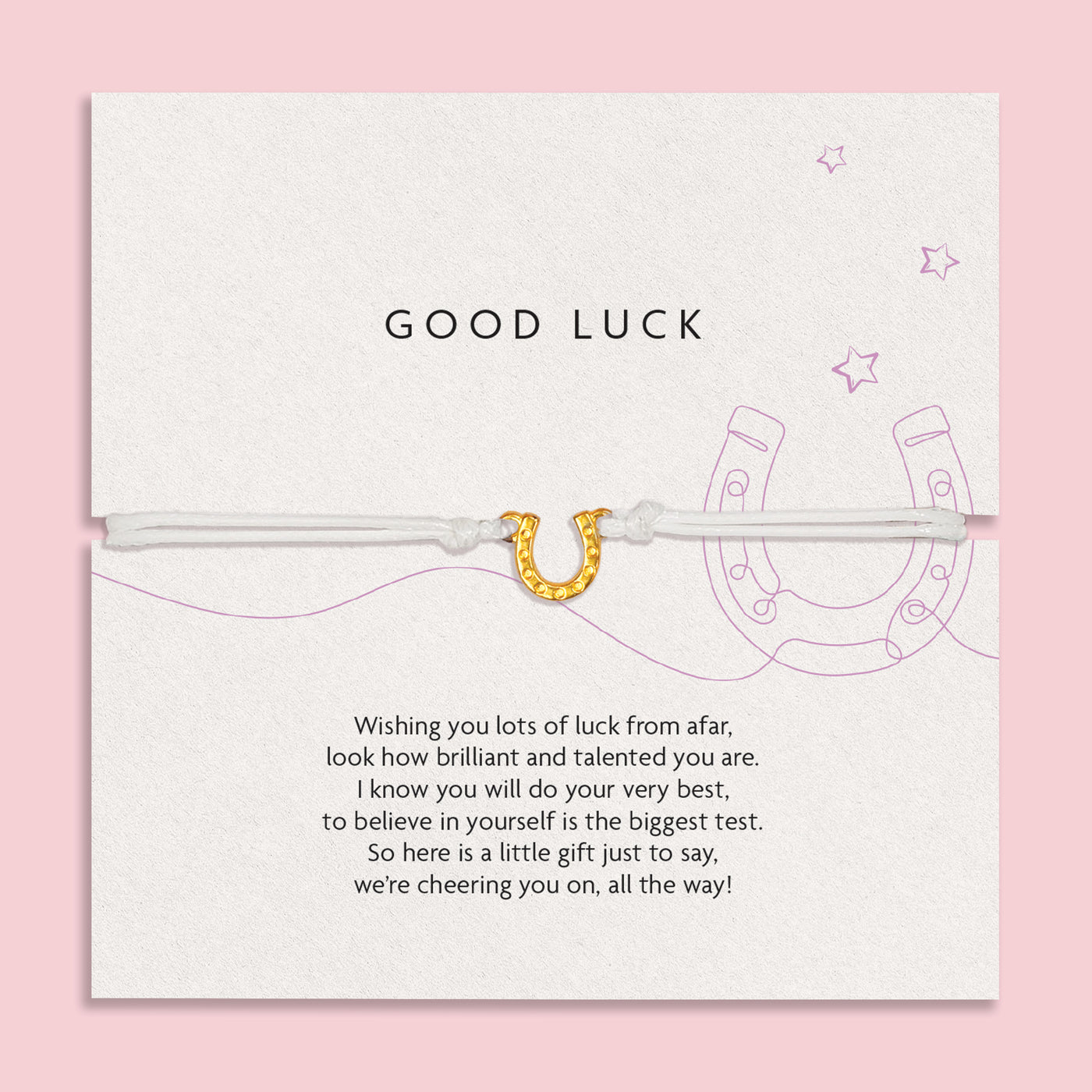 Charming 'GOOD LUCK' card on a soft pink background, adorned with encouraging words and a horseshoe illustration, accompanied by a slender white bracelet with a golden horseshoe charm.