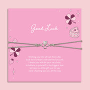 Pink card with 'Good Luck' message and friendship clover bracelet on a pink background