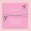 Pink card with 'Good Luck' message and friendship clover bracelet on a pink background