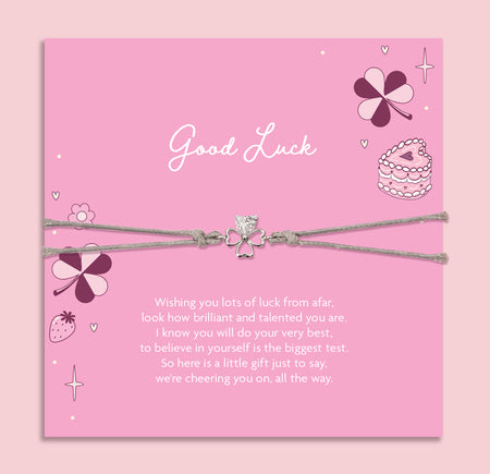 Pink card with 'Good Luck' message and friendship clover bracelet on a pink background