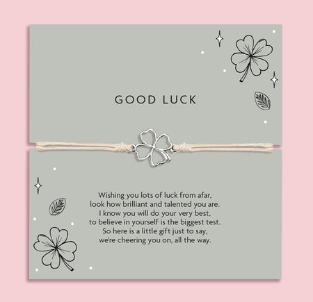 Good luck bracelet with a four leaf clover charm on a card with decorative elements and meaningful poem. The background is pink and the poem card is a green.