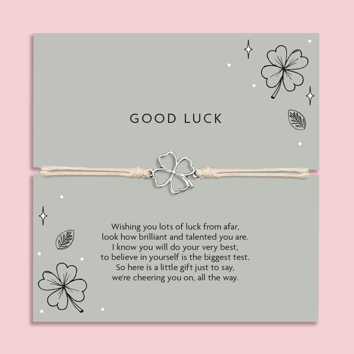 Good luck bracelet with a four leaf clover charm on a card with decorative elements and meaningful poem. The background is pink and the poem card is a green.