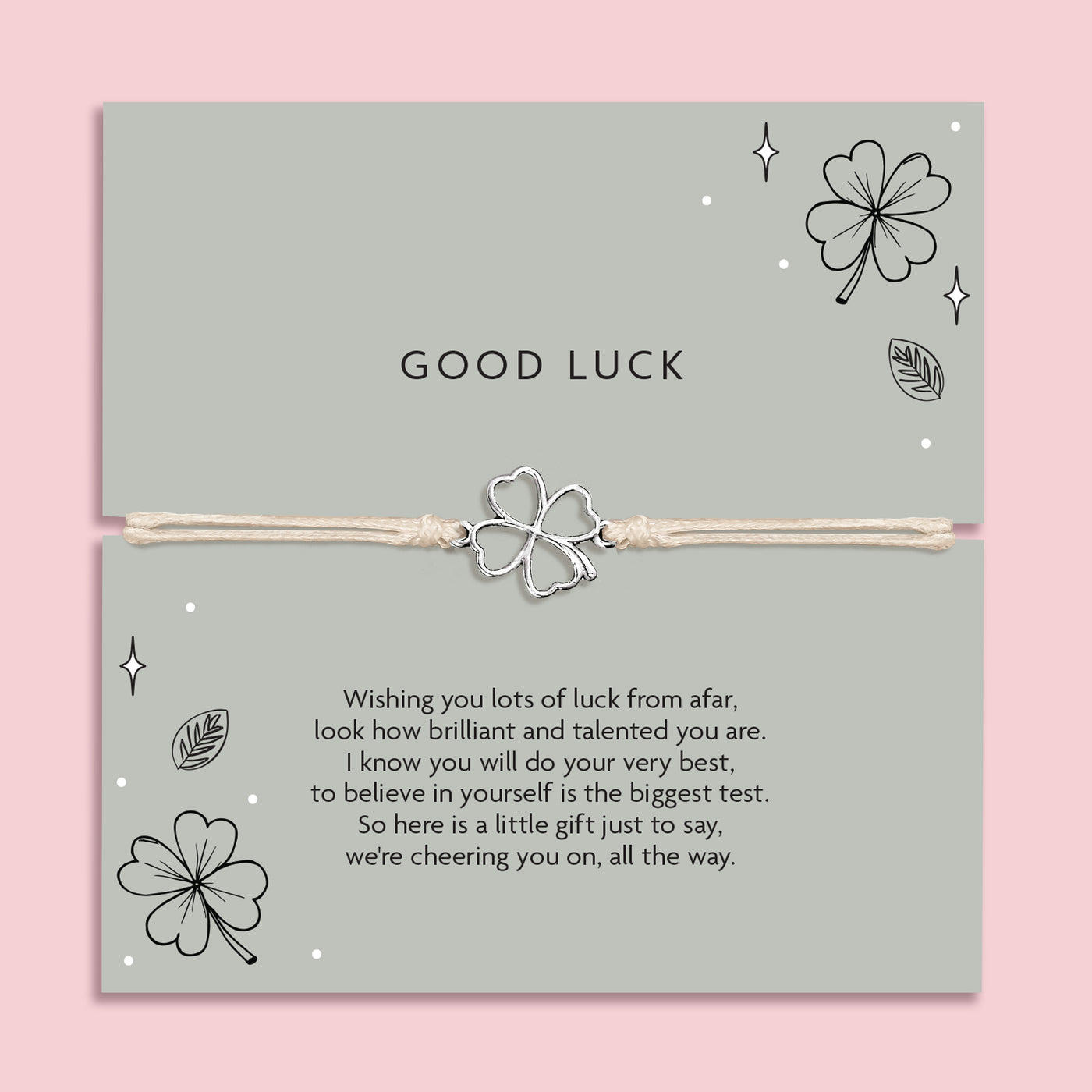 Good luck bracelet with a four leaf clover charm on a card with decorative elements and meaningful poem. The background is pink and the poem card is a green.