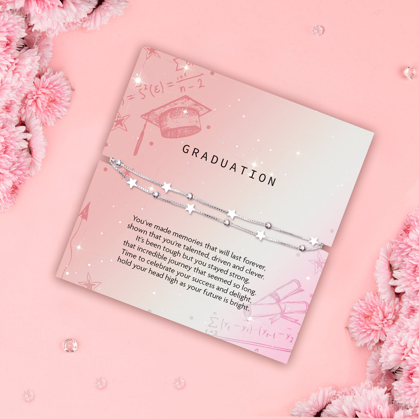 GRADUATION' bracelet with star charms and a solitary pearl, displayed on a soft pink card adorned with illustrations of a graduation cap, arrows, and math symbols. The card carries an uplifting message celebrating a graduate's achievements and bright future.