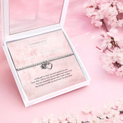 Silver beaded bracelet with heart and flower charms, presented in a white gift box alongside a card titled "Lovely Granddaughter." The card features a heartfelt message celebrating a granddaughter’s special place in your life, filled with love and cheer