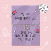 A silver charm bracelet displayed on two lavender gift cards with handwritten-style text and cute doodles, set against a light pink background. One card reads 'To MY GRANDDAUGHTER.
