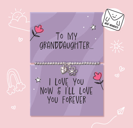 A silver charm bracelet displayed on two lavender gift cards with handwritten-style text and cute doodles, set against a light pink background. One card reads 'To MY GRANDDAUGHTER.