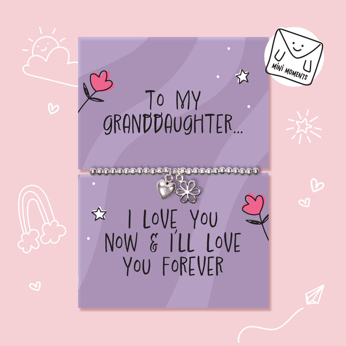 A silver charm bracelet displayed on two lavender gift cards with handwritten-style text and cute doodles, set against a light pink background. One card reads 'To MY GRANDDAUGHTER.