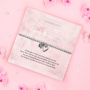 A silver beaded bracelet with a heart and flower charm displayed on a card reading "To my Lovely Granddaughter" from Letterbox Love, set against a soft pink background. The card features a heartfelt poem, making it a perfect gift for a granddaughter to show love and appreciation.