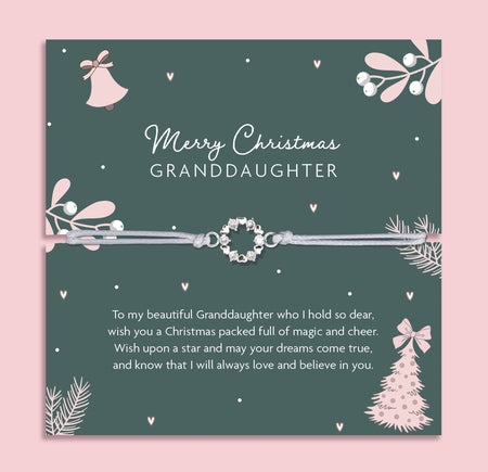 Merry Christmas Granddaughter bracelet featuring a silver wreath charm on an adjustable cord, presented on a festive dark green card with bells, mistletoe, fir branches, and a Christmas tree. Includes a soft white pouch for gifting and safekeeping. A sentimental Christmas jewellery gift for granddaughters of all ages, perfect as a stocking filler, Christmas morning surprise, or heartfelt keepsake from grandparents to celebrate love and family at Christmas.