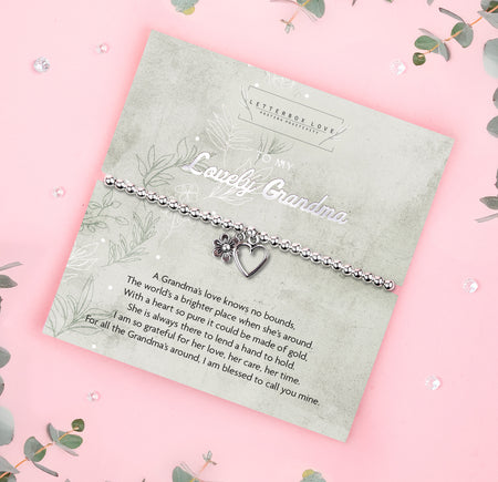 A silver beaded bracelet with a heart and flower charm displayed on a card reading 