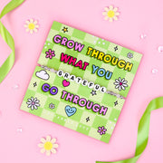 Colourful "Grow Through What You Go Through" grateful bracelet with white letter beads on a vibrant green and pink checked background card, featuring flowers and hearts.