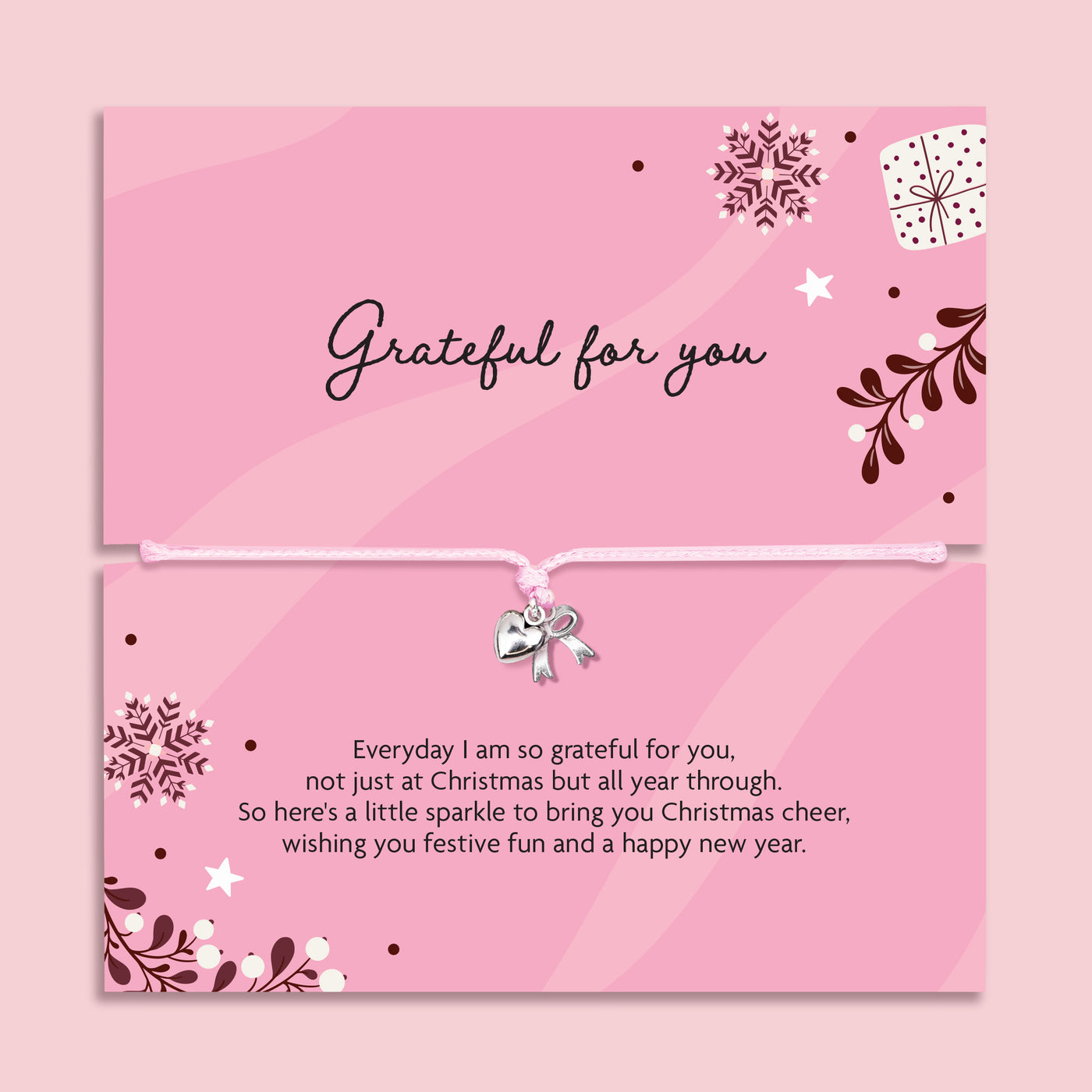 A pink Christmas-themed gift with a top card reading 'Grateful for you' and a bottom card with a message of gratitude, with an adjustable pink cord bracelet and a small silver heart and bow charm. The card features decorative snowflakes, stars, leaves, and a gift box illustration on a soft pink background.