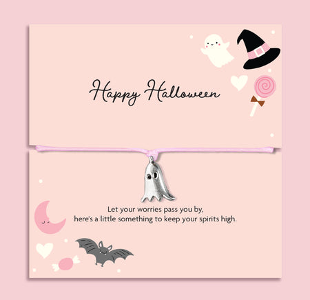 Pink adjustable cord Halloween bracelet with silver plated ghost charm displayed on a pastel pink Happy Halloween sentiment card with spooky ghost, bat, moon and witch hat illustrations.