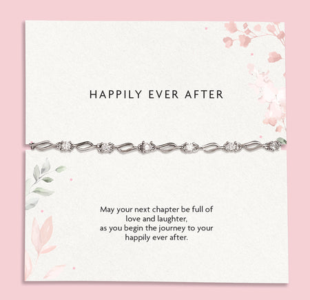 A delicate silver chain bracelet with clear rhinestones displayed on a white card with pink floral accents and the text 'HAPPILY EVER AFTER' and a sentimental message below, set against a solid pink background.