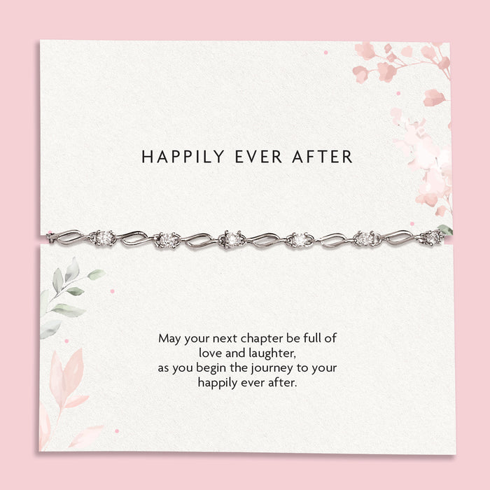 A delicate silver chain bracelet with clear rhinestones displayed on a white card with pink floral accents and the text 'HAPPILY EVER AFTER' and a sentimental message below, set against a solid pink background.