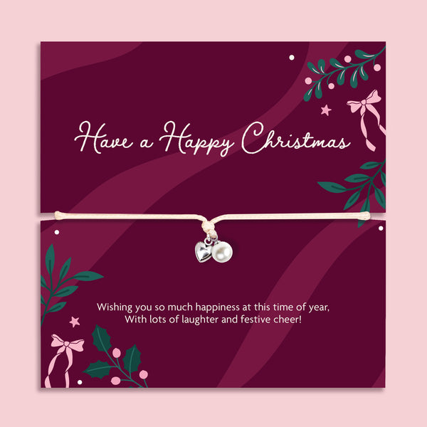 A Christmas-themed poem card featuring a delicate cord bracelet with a silver heart and a pearl charm. The card is deep burgundy with white text reading 'Have a Happy Christmas' and festive green and pink illustrations, set against a light pink background.