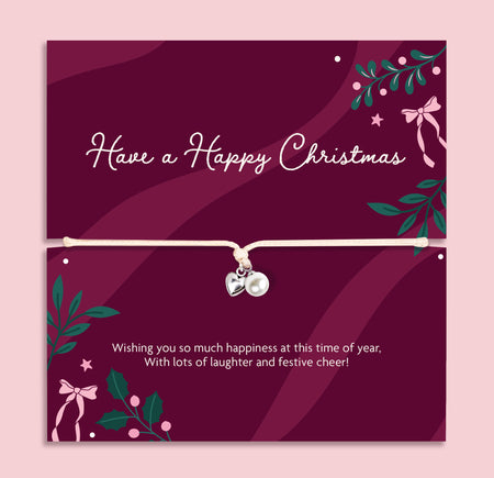 A Christmas-themed poem card featuring a delicate cord bracelet with a silver heart and a pearl charm. The card is deep burgundy with white text reading 'Have a Happy Christmas' and festive green and pink illustrations, set against a light pink background.