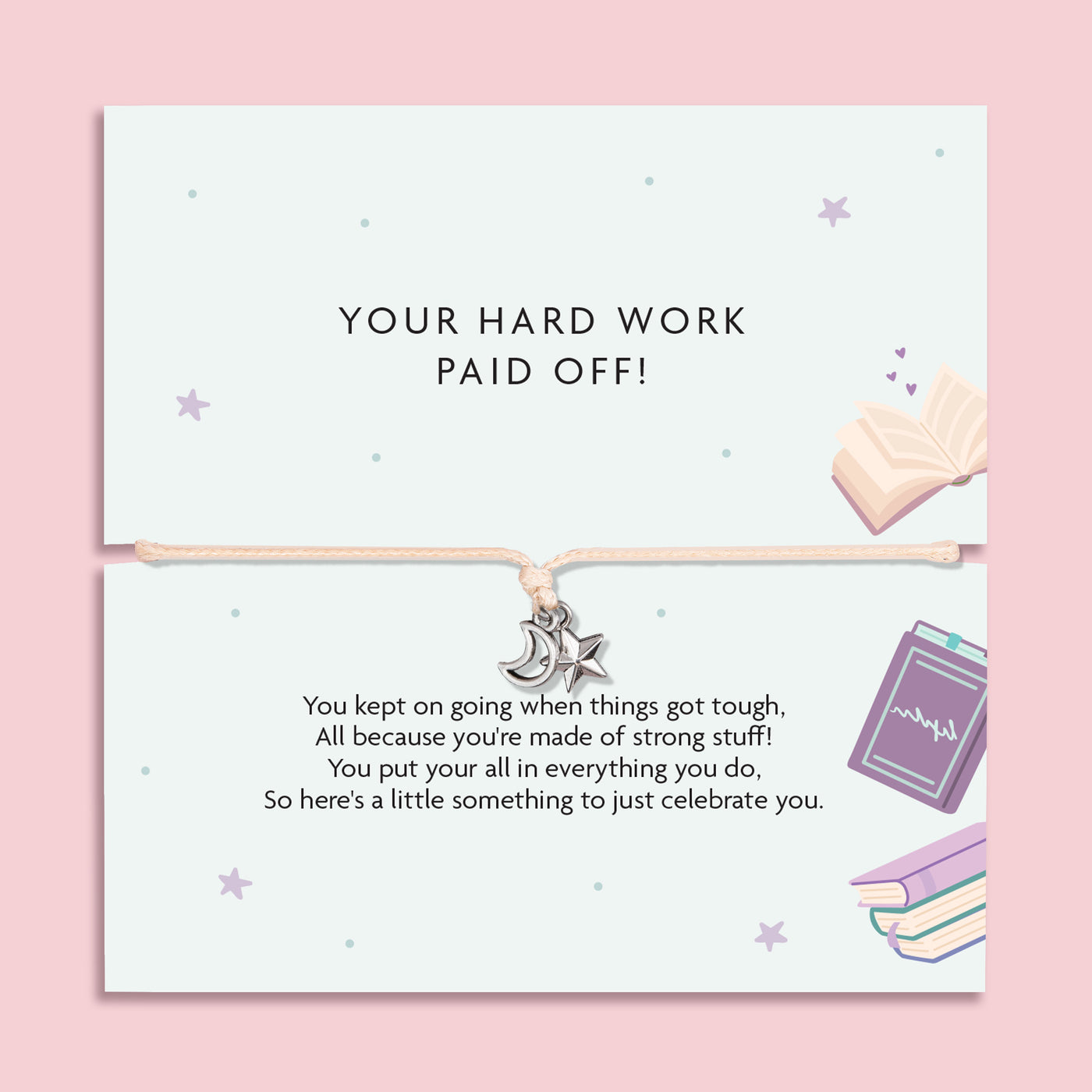 A square greeting card with a thin cord bracelet across the center, featuring a small silver crescent moon and star charm. The top half reads 'YOUR HARD WORK PAID OFF!' and the bottom half has a celebratory message with pastel illustrations of an open book, a notebook, and stacked books on a pink background.