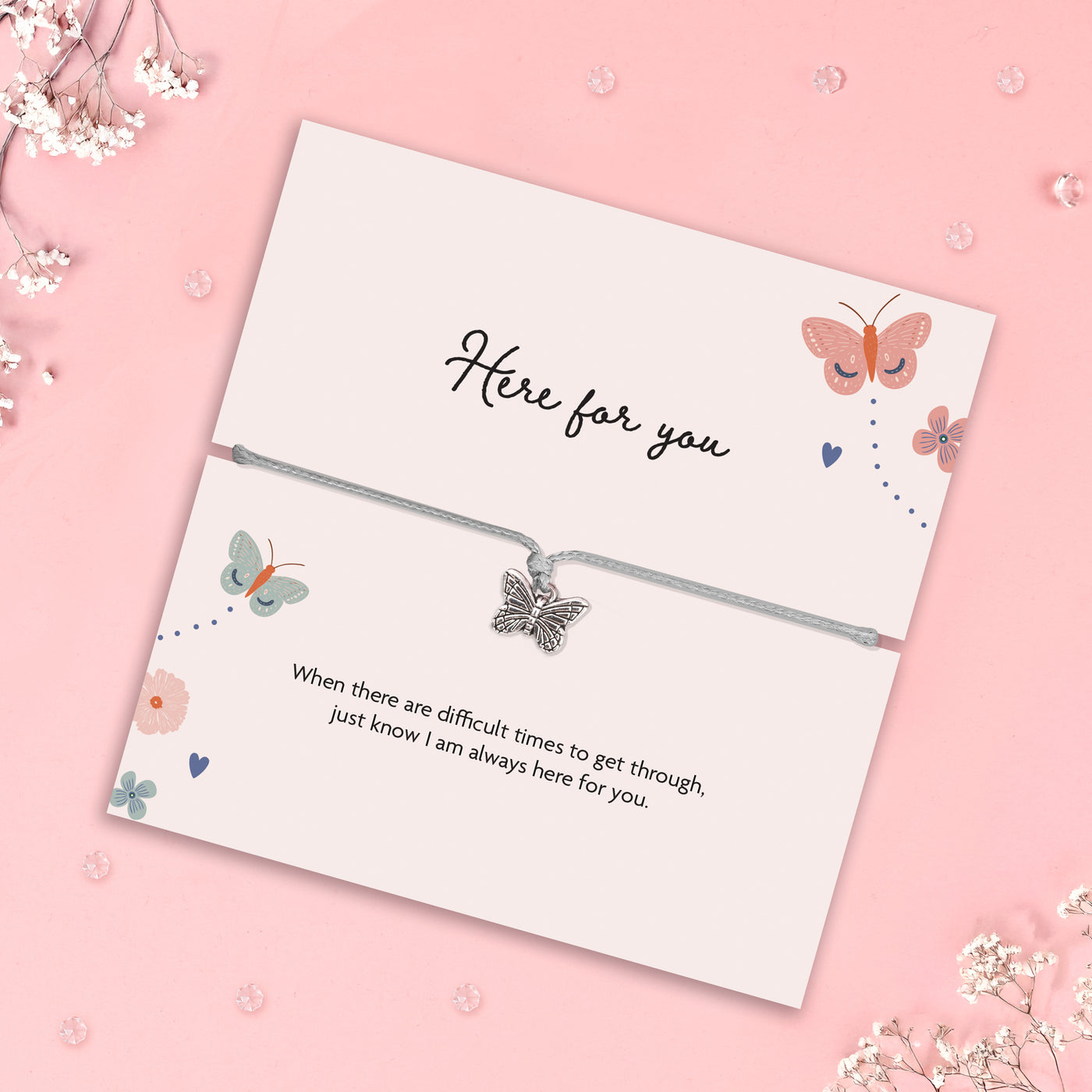 Silver butterfly charm bracelet on a soft grey adjustable cord, presented on a pastel illustrated gift card that reads “Here for you” with a heartfelt message of support, surrounded by delicate butterfly and floral artwork on a pink background.