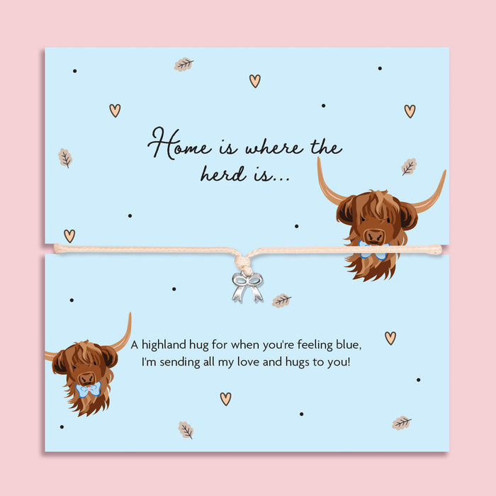 Highland cow bow charm bracelet on illustrated card with two cute Highland cows and the words “Home is where the herd is”, presented as a sentimental gift to cheer someone up.