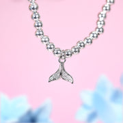 Bracelet with a whale tail charm on a pink background. A silver-plated holiday bracelet with small cubic zirconia gems