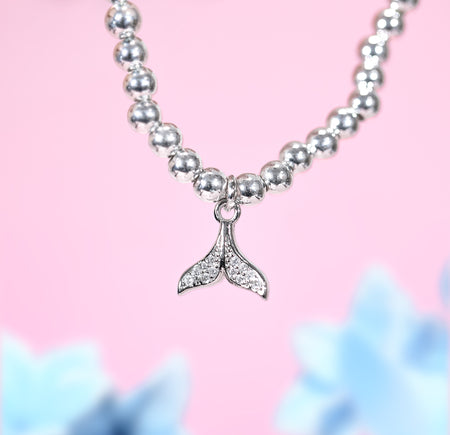 Bracelet with a whale tail charm on a pink background. A silver-plated holiday bracelet with small cubic zirconia gems
