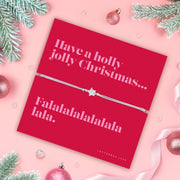Red card with Christmas message and an elegant friendship bracelet on a pink background with festive decorations