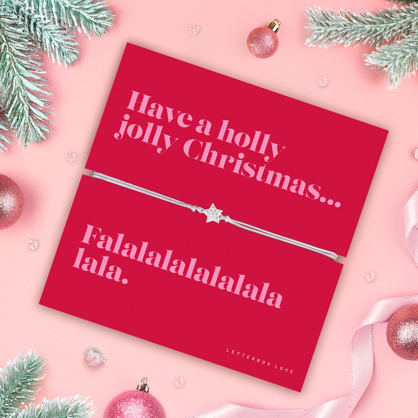 Red card with Christmas message and an elegant friendship bracelet on a pink background with festive decorations