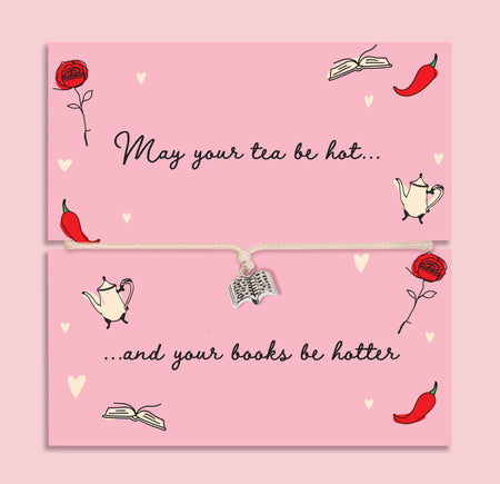 Adjustable string bracelet with small silver book charm presented on pink card reading “May Your Tea Be Hot and Your Books Be Hotter” with illustrated teapots, books and red chillies.