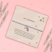 Flat lay of an IVF Journey bracelet gift by Letterbox Love, featuring a beaded silver stretch bracelet with a heart and pineapple charm, displayed on a soft beige sentiment card with floral illustrations and a heartfelt supportive message, perfect for someone undergoing IVF.