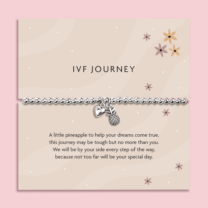 Silver beaded stretch bracelet with heart and pineapple charms on a soft beige sentiment card titled "IVF Journey", featuring floral illustrations and an uplifting message, a supportive gift for someone going through fertility treatment.