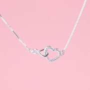 a silver-plated bracelet detail shot of a cubic zirconia hollow heart connecting with an infinity charm on a chain. A cute gift for a daddy and daughter
