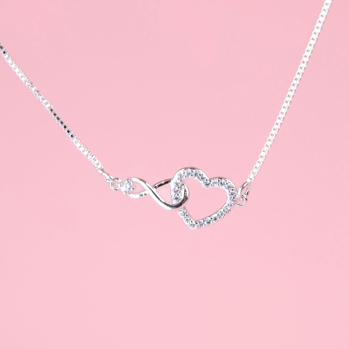 a silver-plated bracelet detail shot of a cubic zirconia hollow heart connecting with an infinity charm on a chain. A cute gift for a daddy and daughter