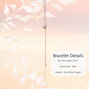 Silver-plated copper box chain bracelet with a sliding closure and small bead accents, shown hanging against a soft peach background with white leaf branches and text detailing the product features.