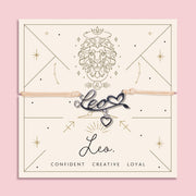 Adjustable beige thread bracelet with a silver 'Leo' charm and heart pendant, displayed on a zodiac-themed backing card featuring a lion illustration and the traits "Confident, Creative, Loyal".
