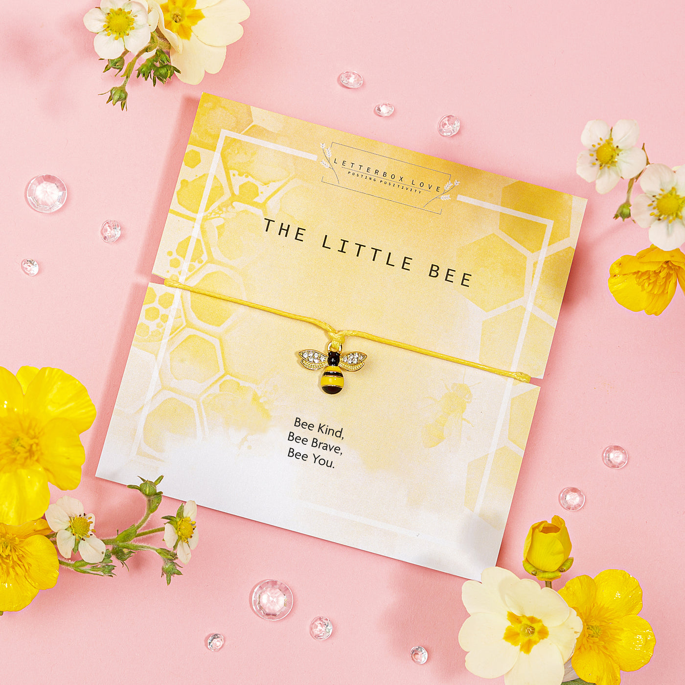 Yellow-themed bracelet card featuring a charming bee charm with sparkling wings, set on a yellow string. The card has a honeycomb pattern background and displays the title 'The Little Bee' along with the inspiring message 'Bee Kind, Bee Brave, Bee You.' Surrounded by yellow and white flowers, this bracelet is a delightful and uplifting gift that encourages kindness and bravery