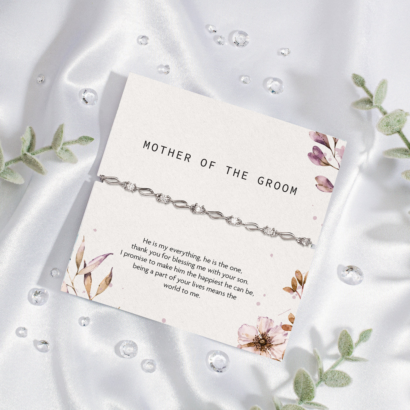 Bracelet with card for 'Mother of the Groom' on a white fabric background with floral elements. The bracelet is a silver-plated, elegant gift for the Mother of the Groom.