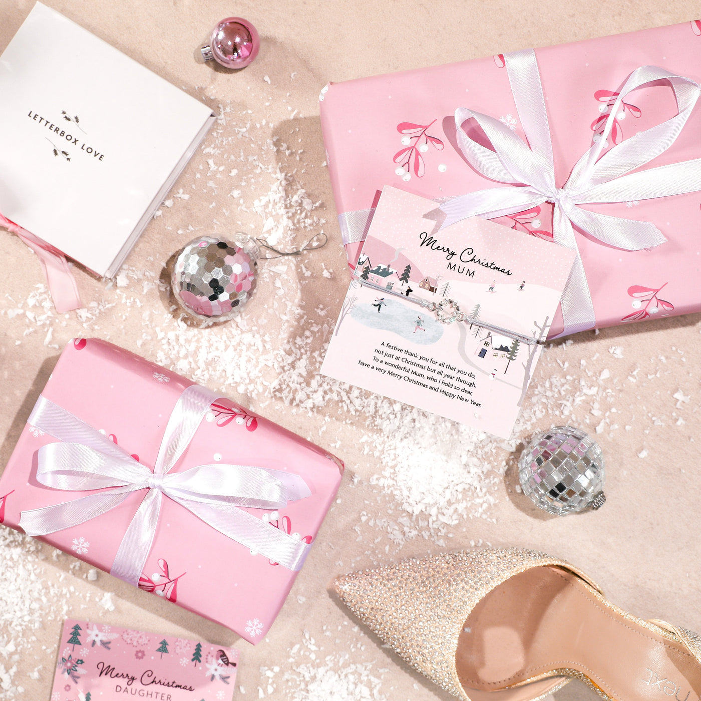 Pink gift boxes with white ribbons on a decorative surface with Christmas cards and disco balls.