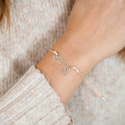 A woman wearing a delicate bracelet with the word “Libra” and a tiny heart charm, a beautiful zodiac bracelet gift for her.
