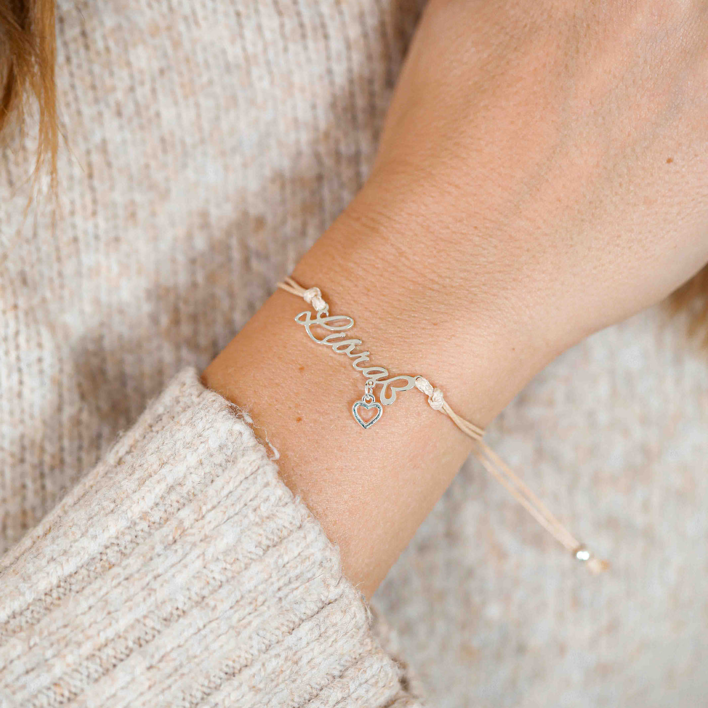 A woman wearing a delicate bracelet with the word “Libra” and a tiny heart charm, a beautiful zodiac bracelet gift for her.