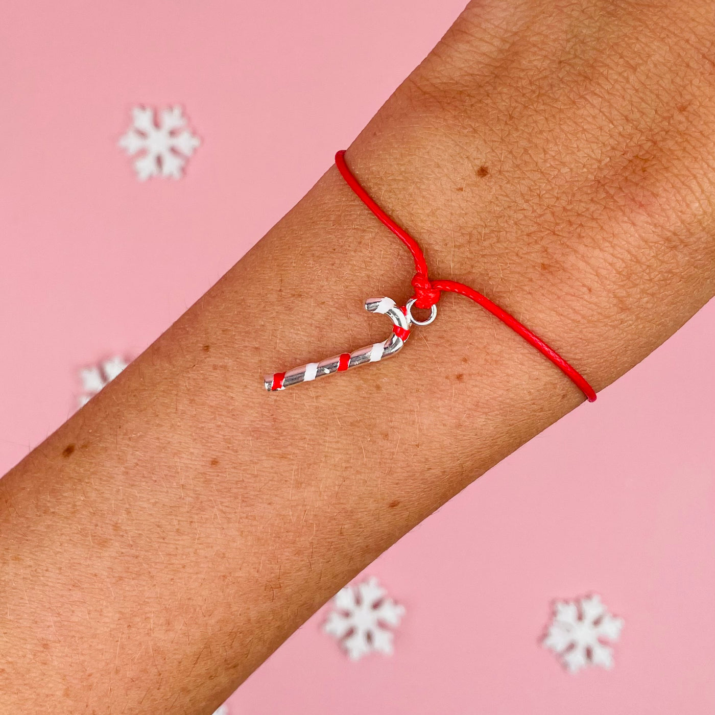 A woman wearing a cute friendship bracelet for Christmas. The charm is a colourful candy cane. The background is pink with white snowflakes.