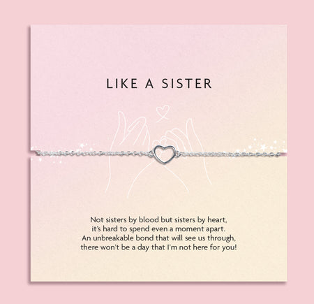 LIKE A SISTER' bracelet featuring a heart charm, presented on a muted pink card with a heartfelt message about the deep bond of friendship that's akin to sisterhood. The card is adorned with delicate pink blossoms and clear crystal gems, set against a soft pink backdrop
