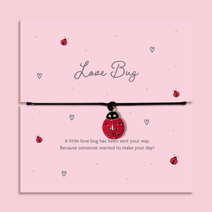 Adjustable black cord bracelet with red ladybird charm displayed on Love Bug message card, cute friendship and thinking of you jewellery gift on pink background.