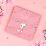 A pink adjustable bracelet featuring an adorable enamel sheep charm, displayed on a pastel pink backing card with the message "I Will Always Love Ewe." Surrounded by soft pink flowers and delicate decorative accents. Perfect for gifting to loved ones.