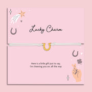 Lucky charm bracelet on a pink card with decorative elements and a horse shoe bracelet