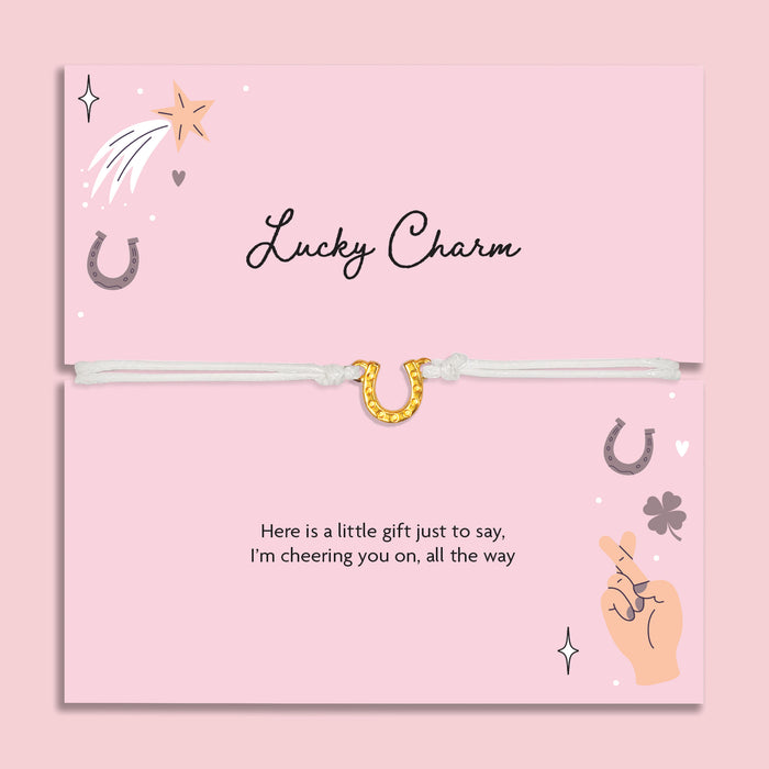 Lucky charm bracelet on a pink card with decorative elements and a horse shoe bracelet